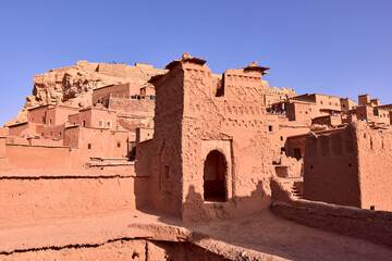 Structures made of earthen materials stand under a cloudless sky in Ait Ben Haddou. Ancient architecture and desert landscape are seen in Morocco.