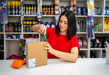 Woman opening delivery package with a utility knife at the counter of an auto parts store