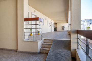 Bright and spacious entrance to a modern building featuring a wheelchair-accessible ramp and well-maintained walkway with potted plants