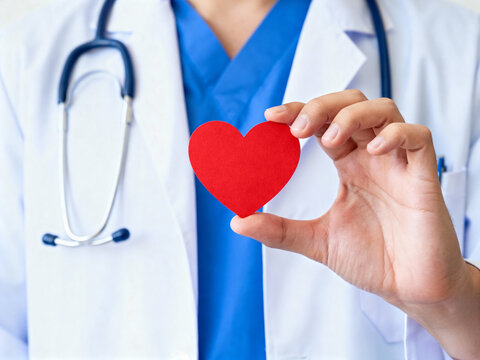 Doctor in white coat holding a red heart shape with stethoscope around his neck in a close up shot
