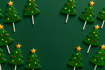 Christmas tree lollipop green candy border with yellow star decorations arranged on dark green background forming a festive holiday frame for seasonal sweet treat themed compositions