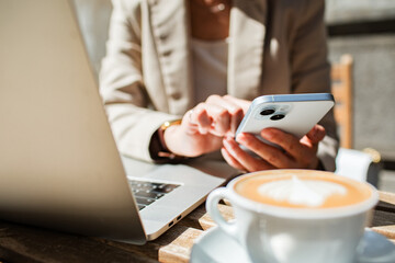 Adult professional using smartphone and laptop at cafe, focused