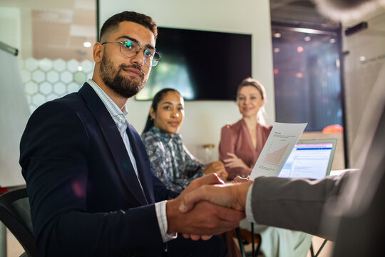 Young adult businessman confident handshake with colleagues in modern office meeting