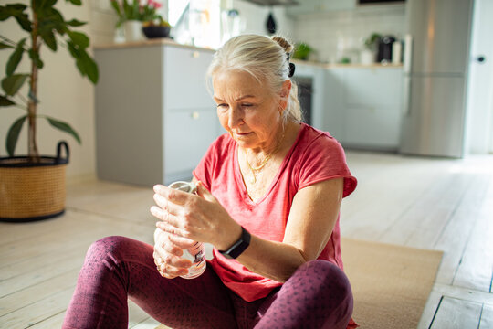 Senior woman hydrating after exercise at home, focused