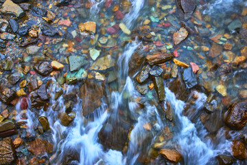 Colorful Riverbed Stones and Flowing Water Cascade in Vibrant Nature Close Up