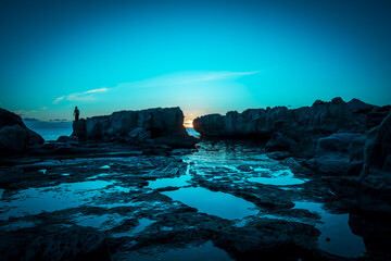 At sunset, a man stands ready to dive, waiting for the right wave on a rock on the island of Favignana, province of Trapani, Sicily, Italy.
