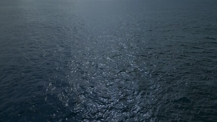 The surface of the blue sea shines thanks to the reflections of the sun, creating a path of light on the surface of the water.