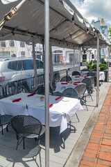 Outdoor restaurant seating under white canopy with empty tables on a sunny day