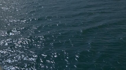 The surface of the blue sea shines thanks to the reflections of the sun, creating a path of light on the surface of the water.