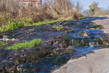 Clear stream flowing over rocky surfaces with green grass and autumn leaves. Natural river environment with bright textures, moss and moving water.