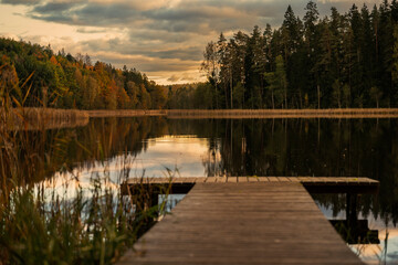 Colourful autumn landscape in the forest next to a lake during sunset, water reflections and colourful sky