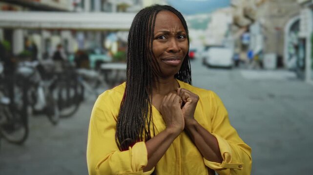 Woman with curly hair in yellow shirt displays surprised expression on urban street with blurred cityscape background during daytime.