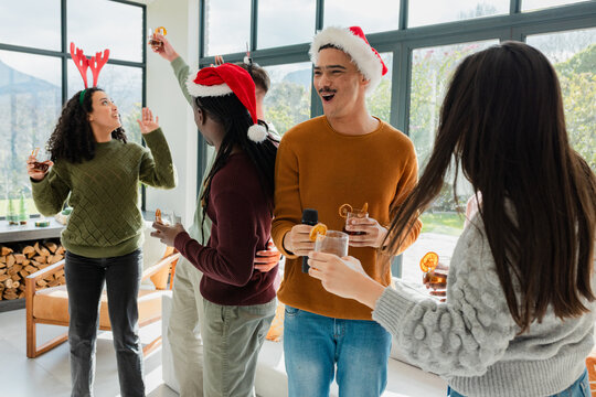 Diverse friends clinking citrus cocktails wearing Santa hats and antler headband in living room