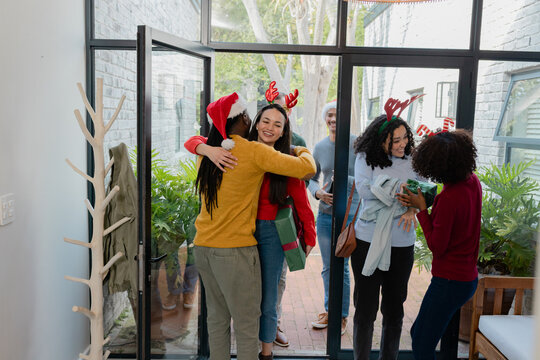 Diverse friends hugging and exchanging gift boxes with Santa hats at modern home entry copy space