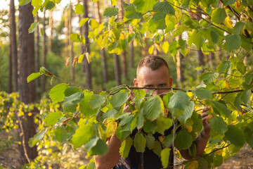 young caucasian man hiding in a green tree foliage