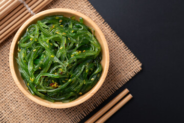 Wakame seaweed salad with sesame seed in a wooden bowl on black background, Top view