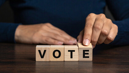 Wooden blocks spelling the word VOTE as a hand reaches out to place the final letter, symbolizing participation in democratic elections and civic duty