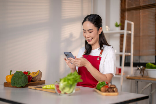 Asian woman cooking healthy meal using smartphone recipe in kitchen - Powered by Adobe