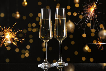 Sparkling wine in glasses on mirror table and festive decor against black background. New Year greeting card