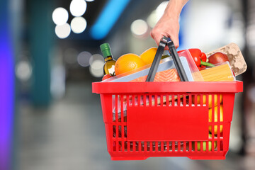 Customer holding shopping basket with different food products at supermarket, closeup © New Africa