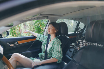 Naklejka premium A young woman sits in the car seat with a calm smile, wearing a green striped shirt and a seatbelt, captured from the passenger side.