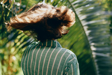 Obraz premium Woman outdoors, back view, striped shirt, wind blows hair, lush greenery, sunny day, fashion moment, natural light, casual elegance, movement, fresh energy, relaxed mood, candid style, outdoor
