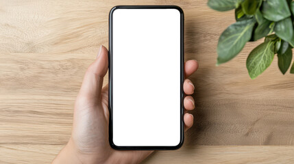 hand holding smartphone with blank white screen on wooden desk, perfect for mockup, app design, and modern presentation visuals