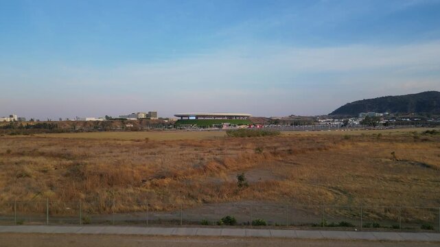 Aerial drone lift-off showing distant Akron Stadium surrounded by dry terrain and urban area