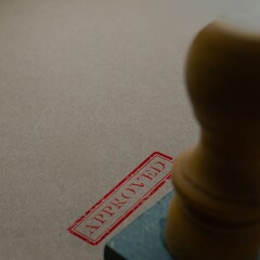 Close-up of a wooden rubber stamp with a red APPROVED mark on brown paper. Validation,...
