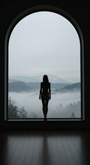 Silhouette of a woman standing by a window overlooking a misty mountain landscape indoors.