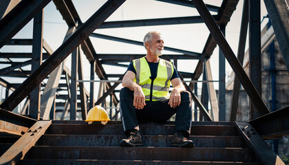 Smiling Senior Engineer Taking Break Sitting on Industrial Metal Stairs