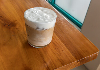 iced coffee latte cappucino with a layer of thick milk foam or whipped cream with a background of a large cafe glass window