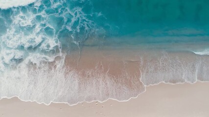 An aerial top-down view of turquoise ocean waves with white foam washing onto a sandy beach.