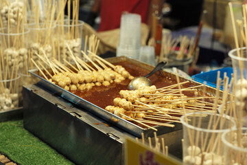 Many pork balls on the bamboo stick dipping in the spicy sauce for selling in the night flea market