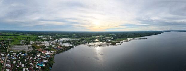 Aerial panoramic view peaceful riverside village in Thailand during sunset featuring calm waters...