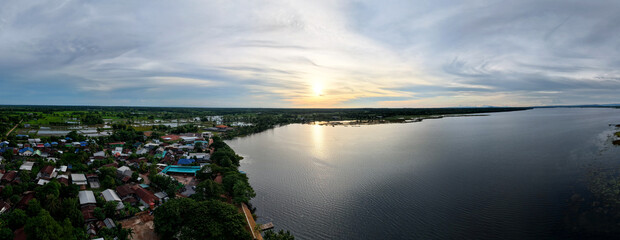 Aerial panoramic view peaceful riverside village in Thailand during sunset featuring calm waters...