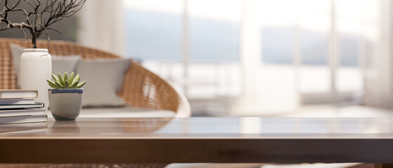 Book and plant aside vase on glass top wooden table across glass wall window in bright living room.