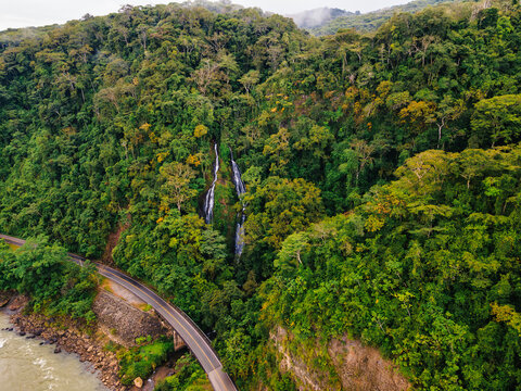 Aerial view of waterfall in lush tropical forest near mountain road - Powered by Adobe