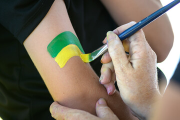 A face painter paints the green and yellow flag on someone's arm for Australia Day - horizontal
