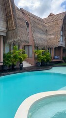 Tropical resort pool surrounded by palm trees and thatched-roof villas under a bright blue sky, creating a relaxing island getaway vibe.