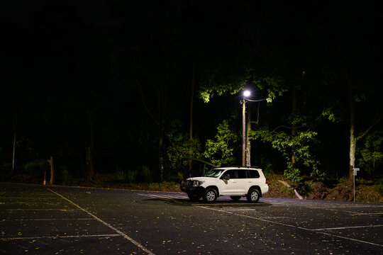 A lone white 4WD car under a street light in an empty parking lot at night - horizontal