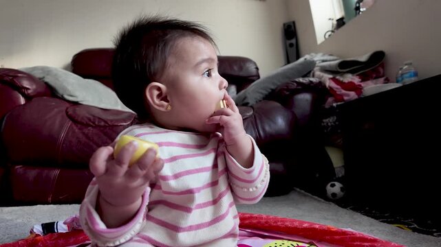 Cute baby chewing on a wooden toy while sitting on a playmat indoors