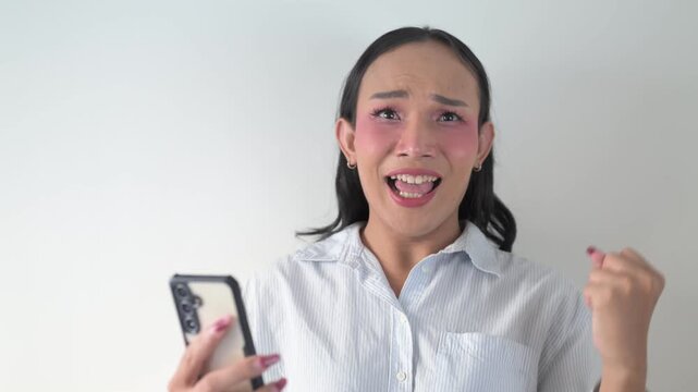 Thai transgender person using smartphone against white background wall indoors getting good news