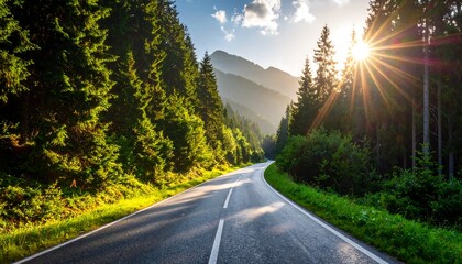 A paved road winds through a lush green forest, sunburst piercing the trees, silhouetting distant mountains