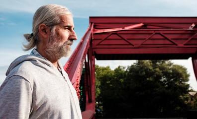 Senior man contemplating near red bridge structure