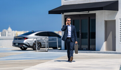 Corporate business. Rich businessman in suit. Business portrait. Successful businessman walking with briefcase in parking. Mature businessman in suit having business call. Rich and independent