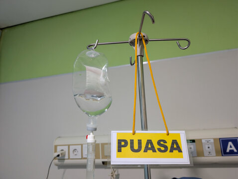 Intravenous (IV) fluid bag hanging on a pole with a yellow sign that reads “FASTING” - Powered by Adobe