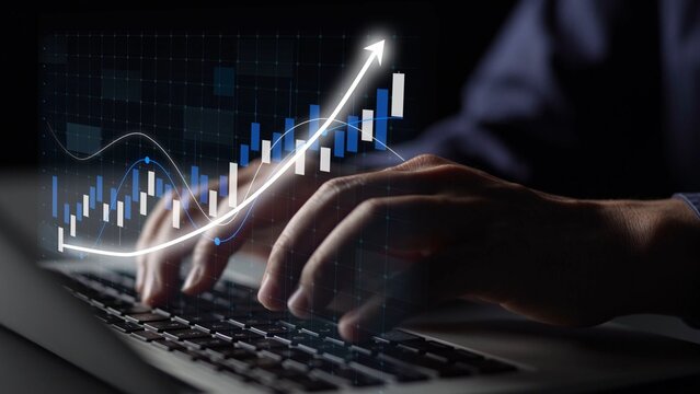 A close-up view of hands typing on a laptop keyboard with a digital financial graph overlay, illustrating growth trends and data analysis in a modern business context. Copula