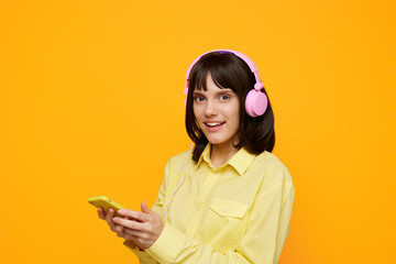 A cheerful young woman wearing a pastel yellow shirt and pink headphones uses a mobile device against a vibrant orange backdrop, capturing a modern, energetic mood.