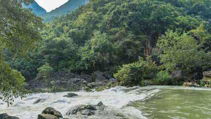 A turbulent mountain river. Streams of white water foam on boulders and rapids. Lush green vegetation on the shore. China. Guiyang. Guizhou.Tianxingqiao Scenic Area